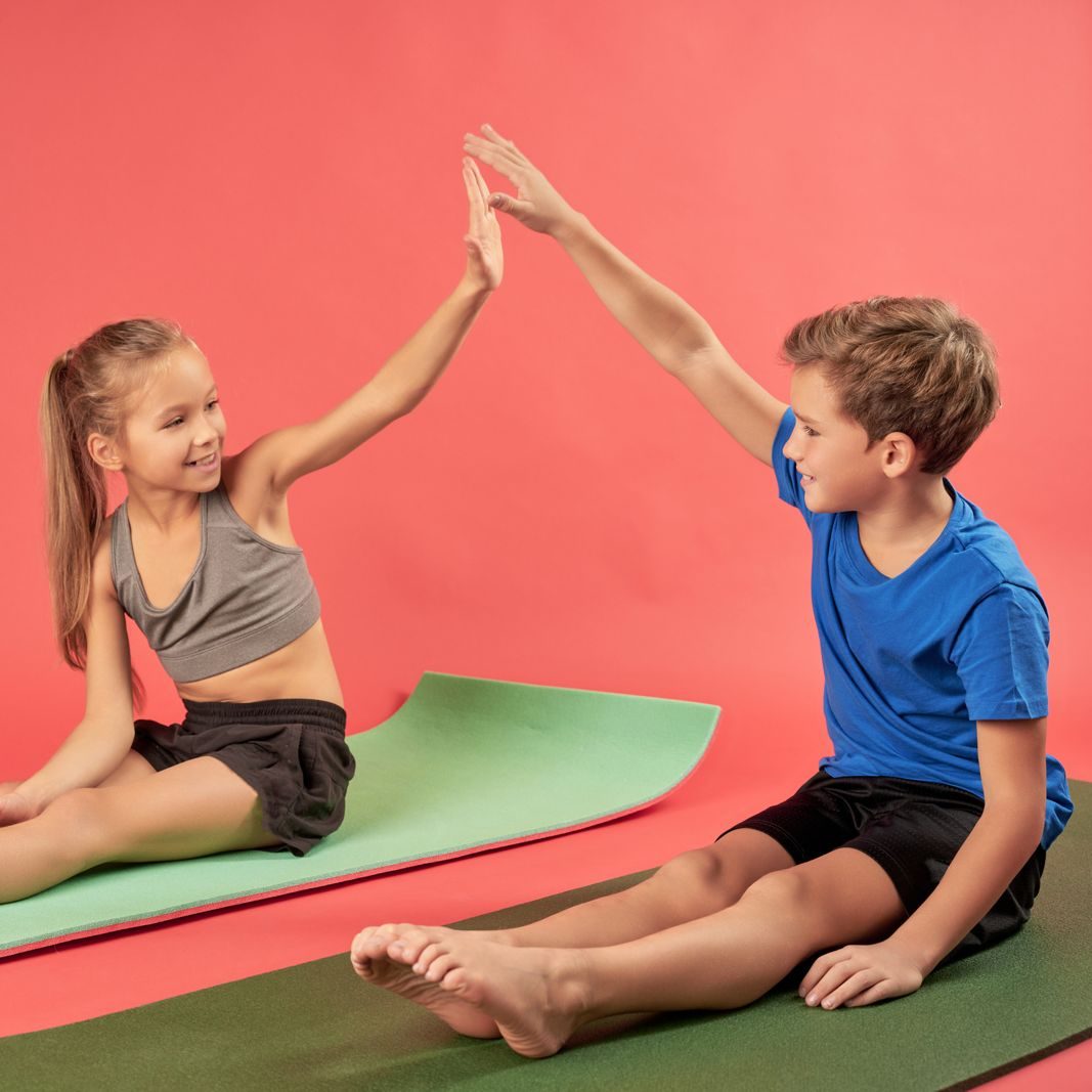 Two children sitting on yoga mats giving each other a high five