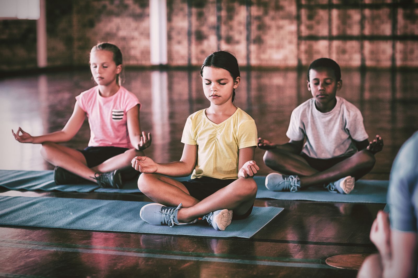 Three children sitting cross-legged on mats with their eyes closed, meditating
